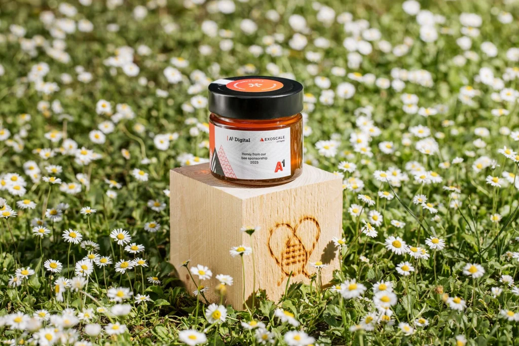 Honigglas im Design von A1 Digital auf einem Holzwürfel mit Zelenka-Brandzeichen in der Blumenwiese