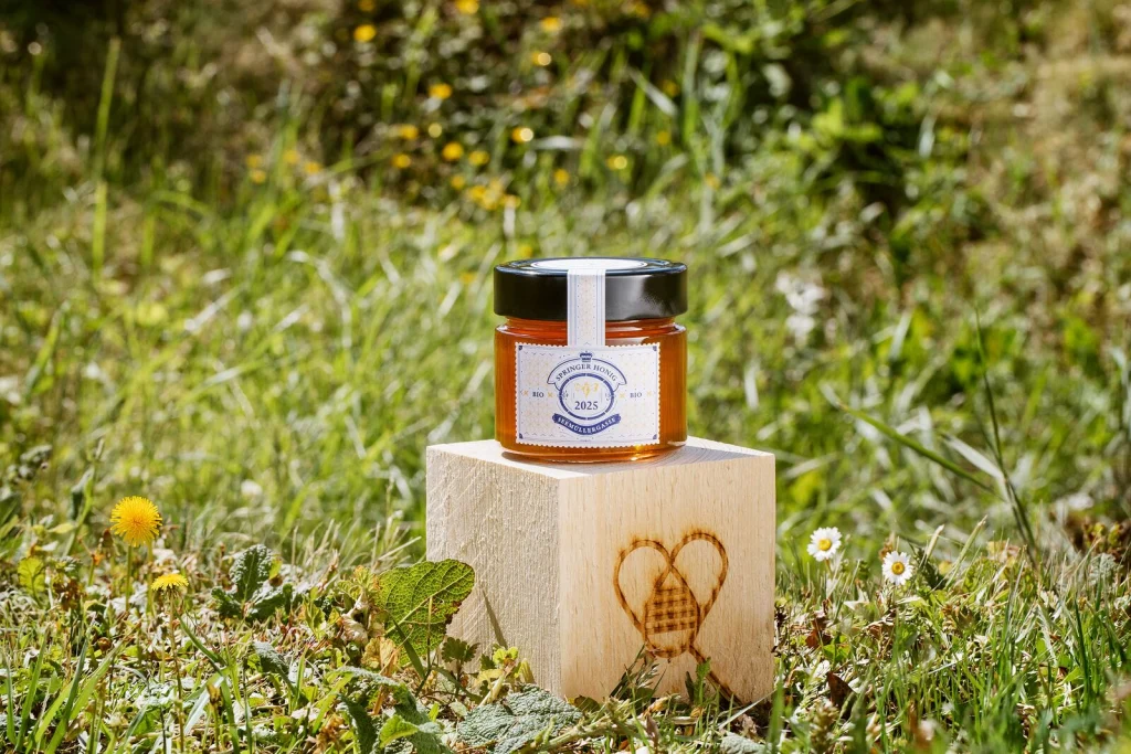 Honigglas im Design von Springer auf einem Holzwürfel mit Zelenka-Brandzeichen in der Blumenwiese